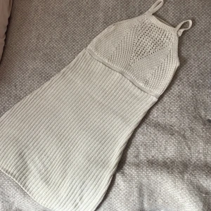 Stickad ljus kortklänning med ribb - Supersöt stickad kortklänning i ljus beige med smala axelband. Överdelen har ett snyggt virkat mönster och kjolen är ribbstickad för en tight passform. 