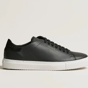 Svarta sneakers från Axel Arigato - Stilrena svarta sneakers från Axel Arigato med vit platt sula och diskret guldfärgad logga på sidan. Skorna har rund tå, snörning och är tillverkade i skinn med detaljer i mocka vid hälen. Perfekta för en clean och modern look. Plus pris kan diskuteras 