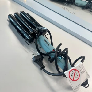 Cosmopolitan Triple Wave Curler - Säljer en Triple Wave Curler från Cosmopolitan i snygg ljusblå färg med svarta värmeplattor. Den har tre cylindrar för att skapa snygga vågor i håret och en enkel on/off-knapp. Perfekt för att fixa beach waves snabbt och smidigt. 
