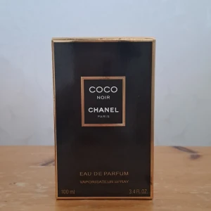Chanel Coco Noir Eau de Parfum 100ml - Lyxig parfym från Chanel, Coco Noir Eau de Parfum i 100 ml flaska. Flaskan är elegant svart med guldiga detaljer och klassisk fyrkantig form. Doften är sofistikerad och mystisk, perfekt för dig som gillar exklusiva och djupa toner.