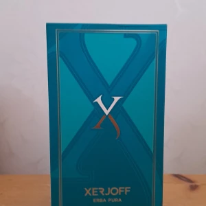 Xerjoff Erba Pura Eau de Parfum 100ml - Lyxig parfym från Xerjoff, Erba Pura, i en snygg blå flaska med gulddetaljer och elegant förpackning. Flaskan har en unik form och exklusiv känsla, perfekt för dig som gillar statement-dofter och vill ha något extra på hyllan.