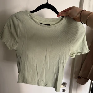 Ljusgrön ribbad topp från Bik Bok - Supersöt ljusgrön ribbad topp från Bik Bok i croppad modell. T-shirten har korta ärmar med vågig kant och rund halsringning. Perfekt att styla med jeans eller kjol för en fräsch look.