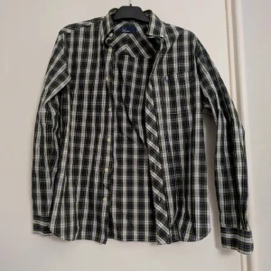 Rutig skjorta från Fred Perry, S - Snygg rutig skjorta från Fred Perry i blått, grönt, vitt och gult. Lång ärm med knappar framtill och bröstficka med broderad logga på bröstfickan. Stilren och tidlös design. Tillverkad i 100% bomull.