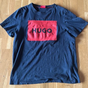 Mörkblå HUGO t-shirt med röd logga - Snygg mörkblå t-shirt från HUGO med stor röd logga framtill. Klassisk rund halsringning och korta ärmar. Tillverkad i mjuk bomull som känns skön mot huden. Perfekt för dig som gillar stilrena plagg med en tydlig logga.