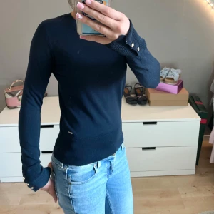 Mörkblå stickad tröja med knappar - Snygg mörkblå stickad tröja med rund halsringning och långa ärmar. Perfekt till jeans eller kjol för en clean och stilren look.