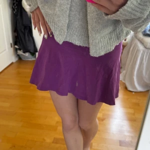 Lila kortkjol från Dolly Style - Superfin lila kortkjol från Dolly Style med broderad logga längst ner. Kjolen har en lätt utsvängd form och är gjord i mjukt bomullstyg som känns skönt mot huden. Köpt men använt bara en gång.