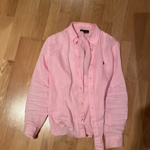 Ralph lauren skjorta  - En rosa Ralph lauren linne skjorta, jag säljer för att den har blivit för liten så jag kan inte ha den. Den är tyvärr lite sliten på armen men annars jätte bra kvalité 