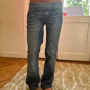 Lågmidjade blå bootcut jeans - Snygga blå jeans med låg midja och bootcut-ben. Jeansen har klassiska fickor fram och bak, samt dubbla knappar i midjan. De är tillverkade i jeansmaterial och har en lätt tvättad look med markerade sömmar. Midjemått: 39cm Står ingen storlek men skulle säga att dem passar en S bra💕💕