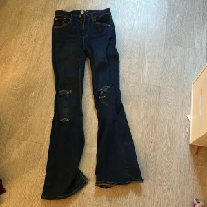 Mörkblå flare jeans från 157 - Mörkblå jeans med flare från 157, modell Snake Flare. Snygga slitningar på båda benen för en trendig look. Klassisk femficksmodell med dragkedja och knapp. Perfekta för dig som gillar retrovibbar och vill sticka ut.