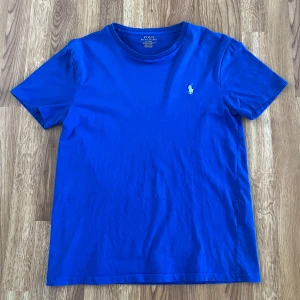 Blå t-shirt från Polo Ralph Lauren - Snygg blå t-shirt från Polo Ralph Lauren med klassisk broderad logga på bröstet. Modellen är slim fit och har rund halsringning samt korta ärmar. Tillverkad i mjuk bomull som känns skön mot huden.