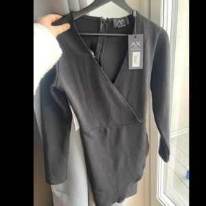 Svart omlottklänning från AX Paris - Snygg svart kortklänning från AX Paris med omlott-skärning och v-ringning. Klänningen har långa ärmar och dragkedja bak. Perfekt för dig som gillar en stilren och elegant look.