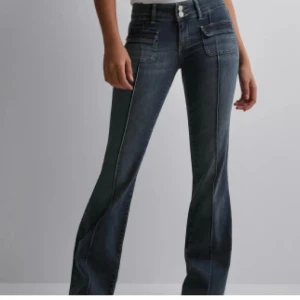 Mörkblå bootcut jeans med fickdetaljer - Snygga mörkblå bootcut jeans med låg midja. Slutsålda och säljs inte längre på hemsidan. Liten defekt på en sidan av jeansen längst upp då flärpen som ska hålla vid ett bälte är lite av 