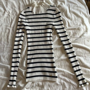 Randig ribbad polotröja i vitt och svart - Supersnygg ribbad polotröja med svarta och vita ränder. Tröjan har lång ärm, hög krage med volangkant och figurnära passform. Perfekt för dig som gillar klassisk stil med en twist. Materialet är stretchigt och mjukt.