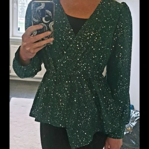 Omlottblus  - Grön omlottblus med silverstänk.  Aymmetrisk skärning och fåll, puffärm och resår i midjan.   Storlek 34/36  Använd vid ett tillfälle, nyskick!   Se gärna mina andra annonser, samfraktar