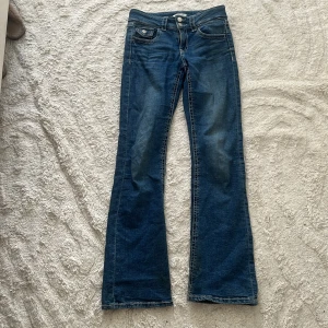 Blå bootcut jeans från Gina Tricot - Snygga blå jeans från Gina Tricot i bootcut-modell med klassiska fem fickor och dubbla knappar i midjan. Jeansen har ljusare tvättade partier och kontrastsömmar som ger en cool look. Perfekta för dig som gillar en retro vibe.