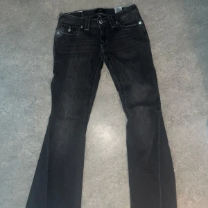 Svarta bootcut jeans True Religion - Säljer ett par svarta jeans från True Religion med bootcut-modell och låg midja . Jeansen har snygga kontrastsömmar, silverfärgade knappar och fickdetaljer både fram och bak. Perfekta om du gillar en klassisk men edgy look.