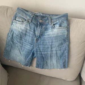 Själv-klippta Blå low-waist jeansshorts  - Snygga ljusblå jeansshorts från SIGGE DESTROYED med råa, fransiga benslut och klassisk femficksdesign. Shortsen har normal passform och är perfekta för sommardagar. Styla med en enkel t-shirt för en chill look.