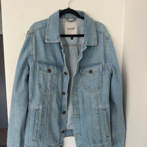 Ljusblå jeansjacka Jack & Jones L - Snygg ljusblå jeansjacka från Jack & Jones i klassisk modell. Jackan har bröstfickor med knappar, raka sömmar och detaljer i kopparfärgad metall. Perfekt oversized fit för en chill look. Materialet är slitstarkt denim och jackan har långa ärmar.