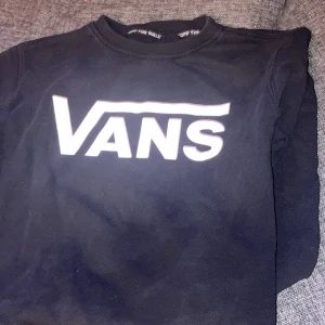 Svart sweatshirt från Vans - Svart sweatshirt från Vans med stort vitt logotryck över bröstet. Klassisk rund halsringning och lång ärm. Perfekt för dig som gillar streetwear och vill ha en enkel men snygg tröja med tydlig branding. Storlek 170