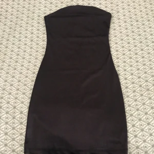 Brun tubklänning från Divided XS - En brun, tight tubklänning från Divided i storlek XS. Klänningen är axelbandslös och har en kort längd med figurnära passform. Perfekt för dig som gillar en enkel och stilren look. Materialet känns mjukt.