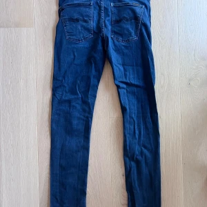 Mörkblå jeans från Nudie - Snygga mörkblå jeans från Nudie med klassiska fem fickor och broderade bakfickor. Jeansen har låg midja och är tillverkade i stretchig bomullsmix för en tight passform. Perfekta för dig som gillar en smal siluett och stilren look.