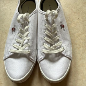 Vita sneakers från Gant i canvas - Använda 1 gång fräscha vita sneakers från Gant i klassisk modell med rund tå och platt sula. Skorna är i canvas med broderad Gant-logga på sidan och har vita snören. Perfekta för en clean och stilren look. 
