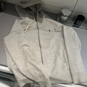  Ralph Lauren zip hoodie - Säljer en stilren grå hoodie från Polo Ralph Lauren med dragkedja och huva. Perfekt för chill dagar och enkel att matcha med jeans. 