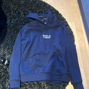 Marinblå hoodie från Polo Ralph Lauren - Snygg marinblå hoodie från Polo Ralph Lauren med broderad vit logga på bröstet. Klassisk känguruficka framtill och huva. Perfekt för dig som gillar stilrena och bekväma plagg med premiumkänsla.Nästan helt ny använd väldigt lite