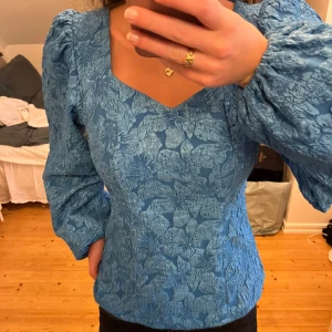 Blommig blå blus med puffärm - Supersnygg blå blus med blommigt mönster och puffärmar. Från ICHI i storlek xs