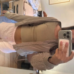 Beige bomberjacka med snörning - Säljer en beige bomberjacka med snygga snörningsdetaljer längs ärmarna. Jackan har dragkedja framtill och ribbade muddar vid ärmslut och midja. Perfekt för dig som vill ha en stilren men ändå unik jacka till din garderob.