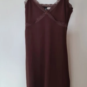 Brun ribbad klänning med spetsdetaljer - Söt brun kortklänning från HM med ribbad struktur, spetskant runt urringningen och en liten rosett framtill. Ärmlös modell med smala axelband och mjuk, stretchig känsla. Perfekt för dig som gillar en enkel men ändå romantisk stil.