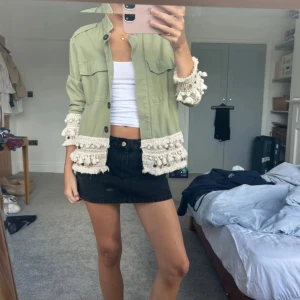 Grön zara jacka (slutsåld) - Snygg ljusgrön overshirt med virkade och fransade detaljer i beige vid ärmslut och nederkant. Jackan har knappar framtill, två bröstfickor och en loose passform. Perfekt för dig som vill sticka ut med coola detaljer och boho-vibe.