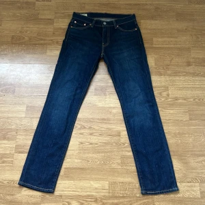 Levi's 511 mörkblå jeans W30 L32 - Säljer ett par Levi's 511 jeans i mörkblå tvätt. Klassisk femficksmodell med smal passform och snygga kontrastsömmar. Jeansen är tillverkade i slitstarkt bomullsjeans och har läderpatch bak i midjan. Perfekta för dig som gillar en clean och tidlös look.