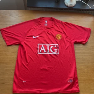 Manchester United Ronaldo 7 Nike XL - Klassisk Manchester United fotbollströja i rött med Ronaldo 7 på ryggen. Tröjan har korta ärmar, broderat klubbmärke på bröstet och AIG som sponsor framtill. Tillverkad i lätt och ventilerande polyester med Nike FitDry-teknologi.
