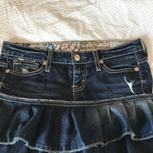 Mörkblå jeanskjol med volang från Guess - Supersnygg mörkblå jeanskjol från Guess med volangkant och slitna detaljer. Jag har sytt den själv då den var ett par jeans innan, den är inte helt felfri men allt syns på bilderna och inget som påverkar funktionen! men skulle man önska en tydligare bild är det bara att skriva 💕Önskas det skulle jag även kunna göra en justering innan jag skickar den🌸 Den har en vintage look och riktigt snygga detaljer. Skriv för mer info💓💓