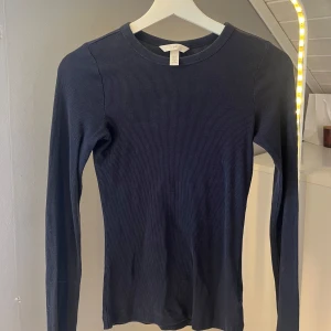 Mörkblå ribbad långärmad tröja H&M - En stilren mörkblå långärmad tröja från H&M i ribbad bomull. Tröjan har rund halsringning och sitter tajt mot kroppen, perfekt att matcha med jeans eller kjol. Enkel och snygg baströja för alla tillfällen. Använd en gång!💓