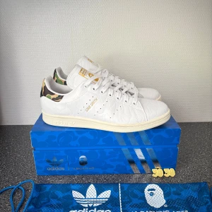 Adidas Stan Smith x BAPE sneakers - Unika Adidas Stan Smith x BAPE sneakers. Köpte fel storlek därav säljer jag dem. Jag har använt dom en gång men de är i helt nytt skick skorna är i storlek 42. Du får med följande: låda, träningspåse extra snören i kamouflage och även guld loggan som ska sitta på snöret längs ner. Pris kan diskuteras 