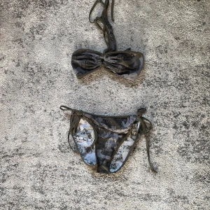 Camo bikini med snörning - Snygg bikini i camouflage-mönster med grå, svarta och gröna toner. Överdelen är bandeau-modell med knyt i nacken och baktill, medan underdelen har knyt i sidorna. Perfekt för stranden eller poolen och ger en cool vibe.
