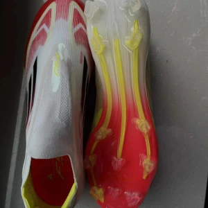 Adidas F50 elite - Säljer ett par Adidas F50 fotbollsskor i vitt med röda och gula detaljer samt svarta ränder på sidorna. Skorna är inte använda har haft på de nån gång. Nypris på 3000 kr då de är den bästa modellen. Skorna har en strömlinjeformad design utan snörning och en lätt syntetisk ovandel. Sulan är röd och gul med fasta dobbar för bra grepp på planen.