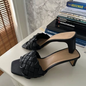 Svarta flätade klack-sandaler H&M - Använd 1 gång. Stilrena svarta sandaler från H&M med låg klack och fyrkantig tå. Ovandelen har en bred, flätad rem i syntetmaterial som ger en trendig look. 