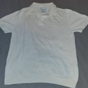 Vit stickad pikétröja från Vailent - Vit stickad pikétröja från Vailent i linnemix. Klassisk krage med två knappar och korta ärmar. Tröjan har en clean och stilren look, perfekt för dig som gillar en enkel men snygg stil. Ribbad kant nedtill och vid ärmslut.