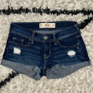 hollister shorts - Snygga mörkblå jeansshorts från Hollister med låg midja, slitna detaljer och uppvikta benslut. Perfekta för varma dagar och en avslappnad stil.