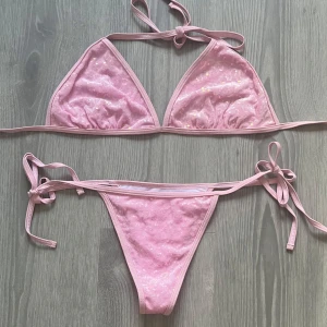 Rosa glittrig bikini med snörning - Söt rosa bikini med glittriga paljetter och smala band som knyts i sidorna och runt nacken. Triangelformad överdel och klassiska bikinitrosor. Perfekt för strandhäng och poolparty. Bikinin är aldrig använd, endast provad! 