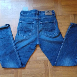 Blå Replay jeans straight fit - Säljer ett par stilrena blå byxor från Replay i storlek 158cm. De har en klassisk design med knappar och är perfekta för vardagar eller fest. Materialet känns slitstark och bekvämt. Passar bra till höst- och vårsäsongen. Perfekt för dig som vill ha en snygg mångsidig byxa! Hör av er vid frågor och snabb affär