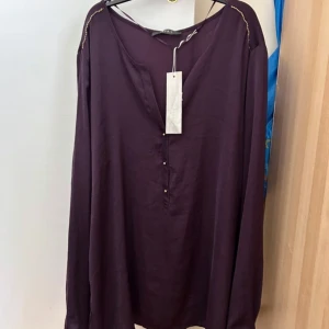 Lila blus med gulddetaljer från Esprit - Snygg lila blus från Esprit med v-ringning och guldfärgade knappar framtill. Långa ärmar och dekorativ guldfärgad söm längs axlarna ger en extra touch. Luftigt material som känns skönt mot huden. Perfekt för dig som gillar stilrena men unika plagg.