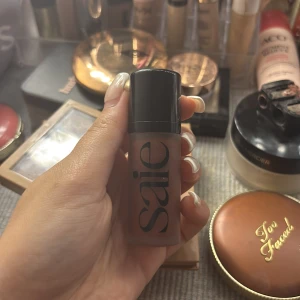 Saie flytande bronzer - Flytande bronzer från Saie i en snygg brun nyans. Kommer i en frostad glasflaska med svart lock och stor logga på framsidan. Perfekt för att ge ansiktet en solkysst look och enkel att blenda ut för ett naturligt resultat.