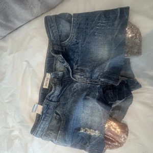 Blå jeansshorts med paljett-detalj - Snygga blå jeansshorts från Sally & Circle med råa kanter och slitningar framtill. På insidan syns en glittrig paljett-detalj i silver som sticker ut under shortsen. Klassisk femficksmodell och normal passform. Perfekta för sommaren!