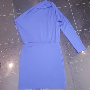 Blå one shoulder klänning - Snygg blå kortklänning från Bik Bok med one shoulder-design och lång ärm. Klänningen har en cool draperad detalj vid axeln och är figurnära i modellen. Perfekt för dig som vill sticka ut med en trendig look. PRIS KAN DISKUTERAS!