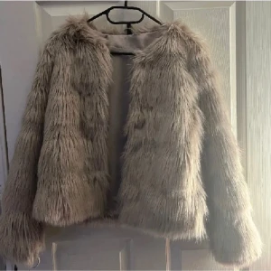 Beige pälsjacka med lång ärm - Snygg beige pälsjacka med lång ärm och fluffig känsla. Jackan har en croppad passform och är perfekt för dig som vill sticka ut med en trendig look. Fodrad insida för extra komfort. Passar till många olika outfits. Pälsen är mer fluffig och håller ihop mer:)
