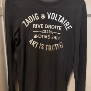 Svart långärmad tröja Zadig & Voltaire - Svart långärmad tröja från Zadig & Voltaire med tryck i silver på bröstet där det står 'Art is truth' och 'Rive Droite'. Tröjan har rund halsringning och är tillverkad i mjuk bomull, perfekt skick.